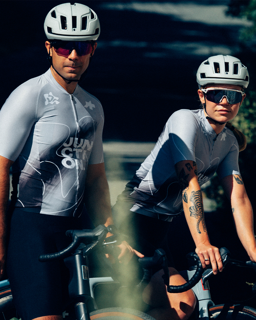 Two riders in the Junction Pathfinder jersey standing over road bikes at dusk